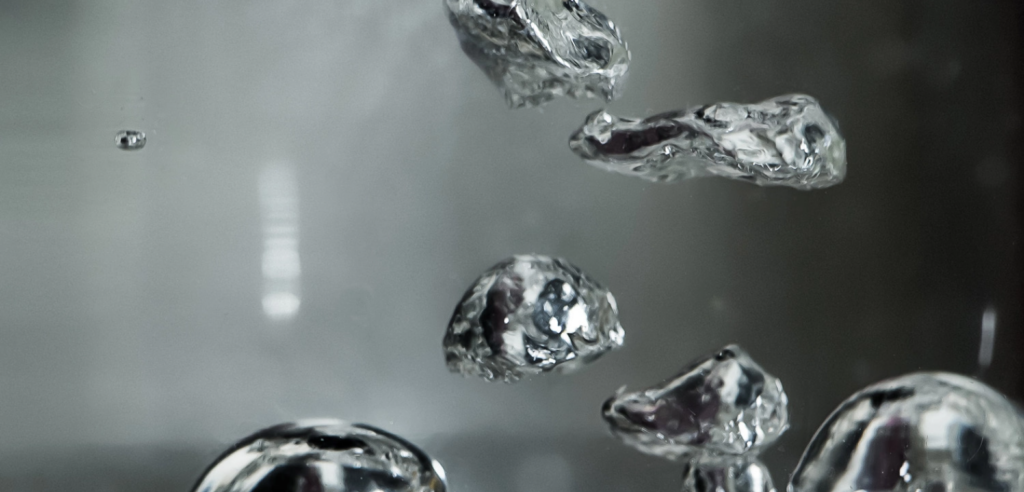 Crumbled aluminum foil pieces floating in a clear liquid, reflecting light from all sides.] ,