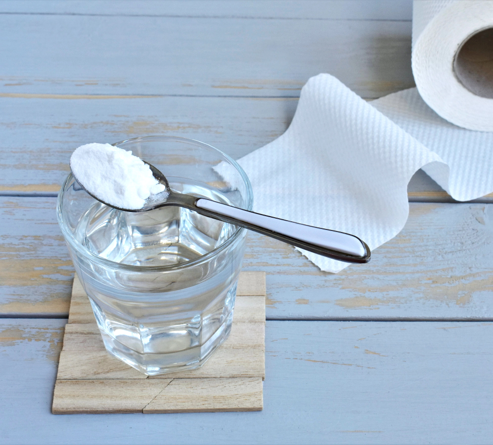 Spoon with white powder over a glass of water on a wooden coaster with a roll of toilet paper in the background.